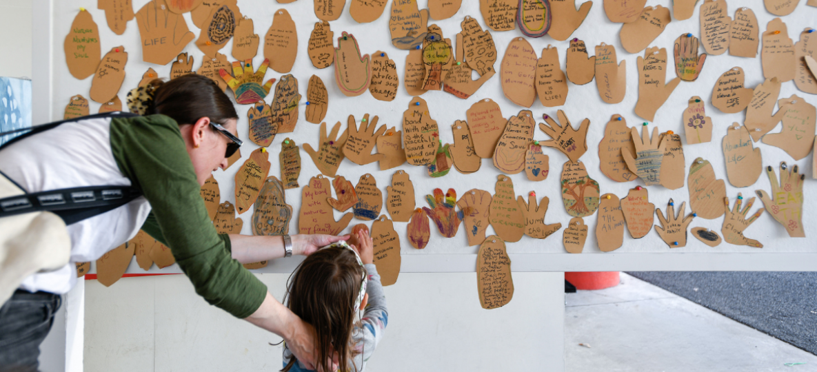 young girl and mother adding paper hand to community art board