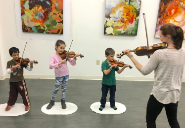 three young violin students playing with a teacher