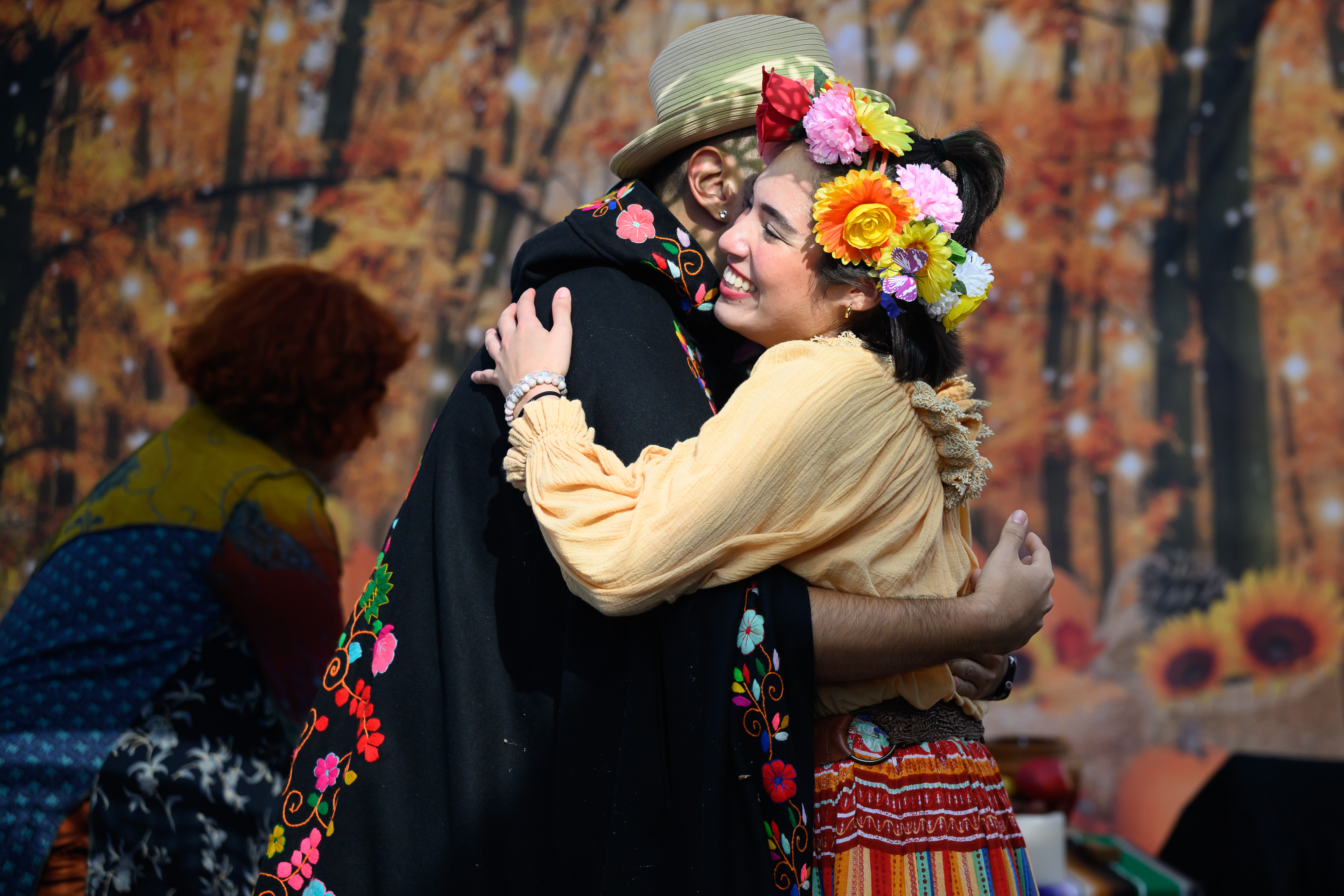 Performers hug in front of an autumn backdrop