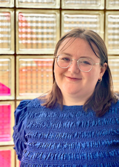 Staff portrait of young adult female with brown hair and glasses wearing a royal blue top.