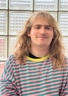 Staff portrait of young adult with blonde medium length hair wearing a striped sweater.