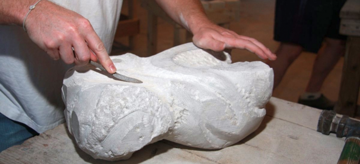 Stone carver working with a large piece of white stone and a carving tool.