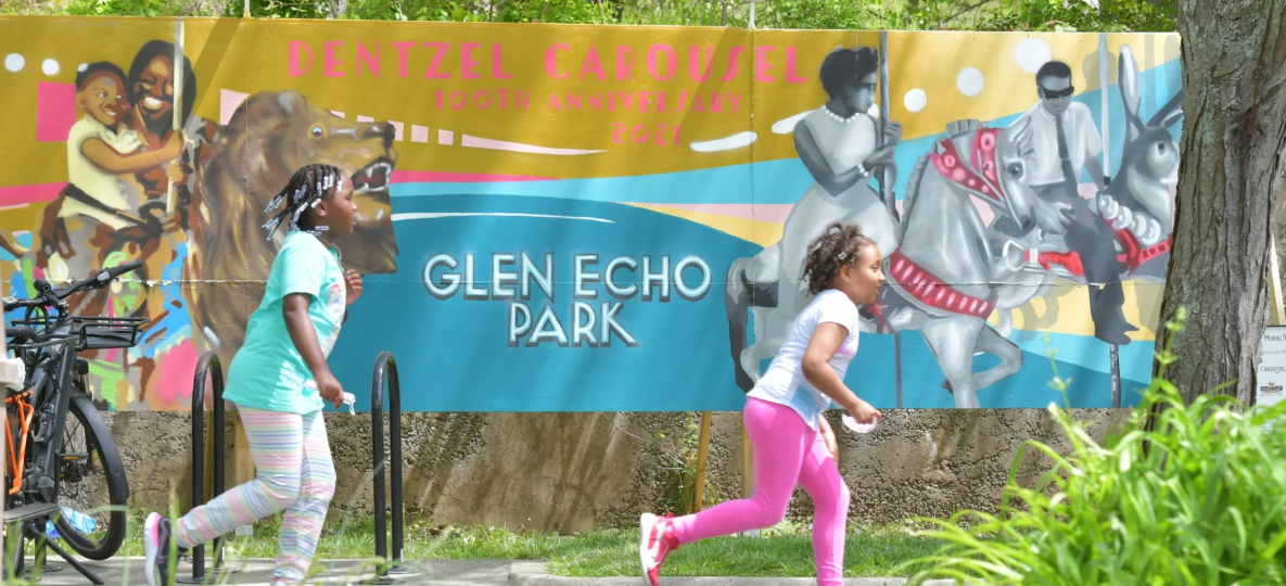 Children run past a mural of carousel riders