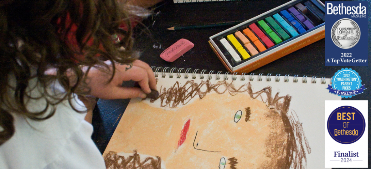 girl drawing self portrait with oil pastels; local award symbols for children's classes
