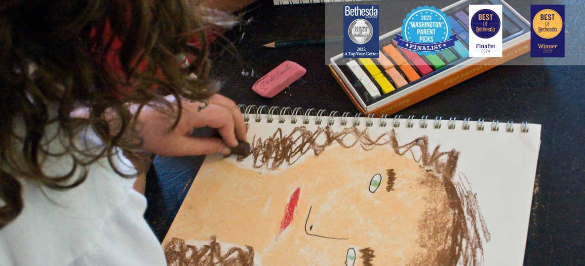 girl drawing self portrait with oil pastels; local award symbols for children's classes