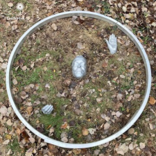 An outdoor sculpture of hands and a face emerging from the ground