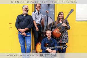 An image of Rusty Sal standing against a yellow brick wall with their instruments