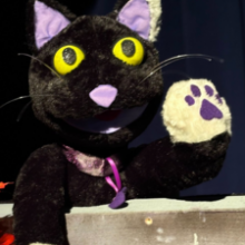 Jennie the cat, a black cat puppet, waves her hand