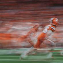 long exposure photo by Elizabeth Billman of football players in orange and white uniforms running on field
